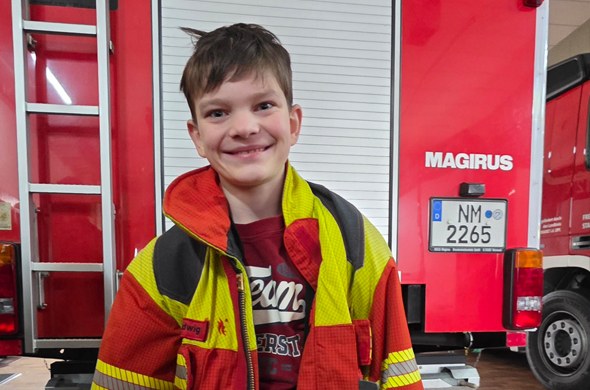 Schüler mit Feuerwehrjacke steht in Feuerwehrhalle