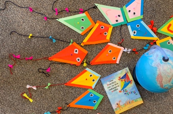 kleine gebastelte Papierdrachen liegen neben einem Buch und einem Globus auf dem Boden