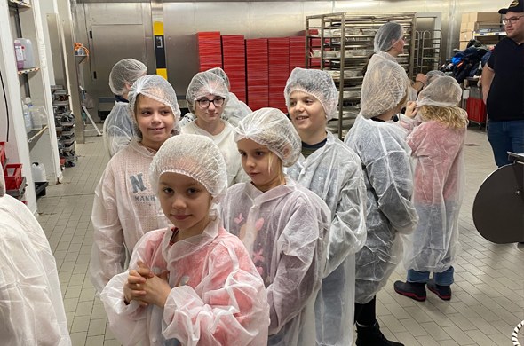 Schulkinder mit Hygienekopfbedeckung und Umhang stehen in der Backstube