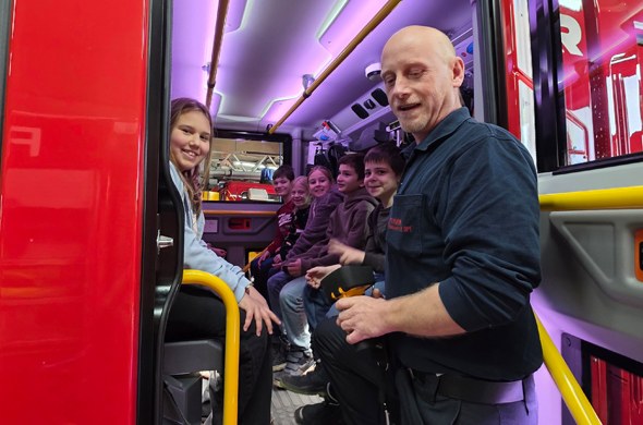 Schüler sitzen im Feuerwehrbus vorne steht Feuerwehrmann auf Trittbrett