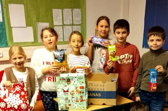 Schulkinder mit gespendeten Geschenken stehen an Tisch