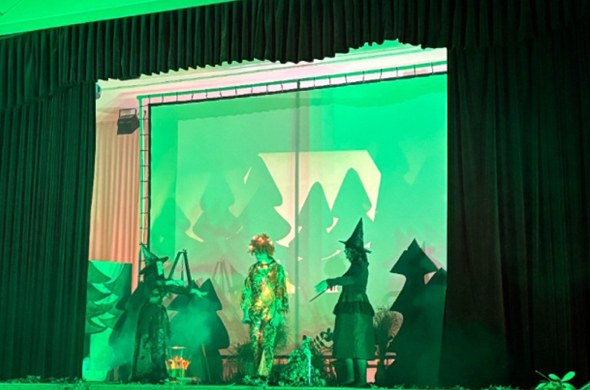 Eine grün beleuchtete Bühne mit Schülern präsentieren Szene aus Theaterstück
