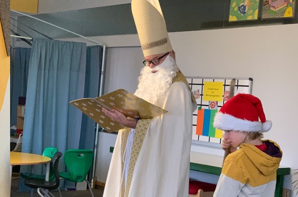Nikolaus liest aus goldenem Buch daneben Kind mit Nikolausmütze
