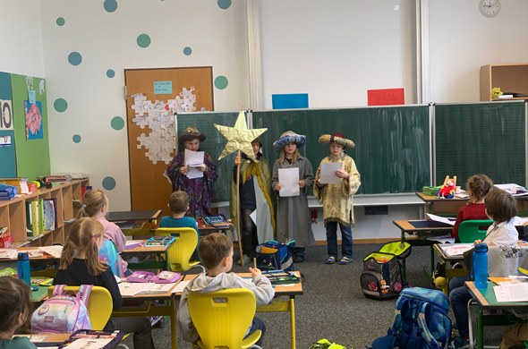 Vier Sternsinger stehen in Klassenzimmer vor der Tafel und tragen etwas vor