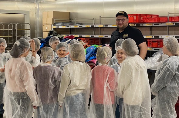 Schulkinder in Hygienekleidung stehen beim Bäckermeister