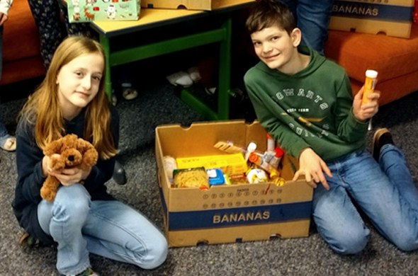 Schulkinder mit gespendeten Geschenken sitzen am Boden