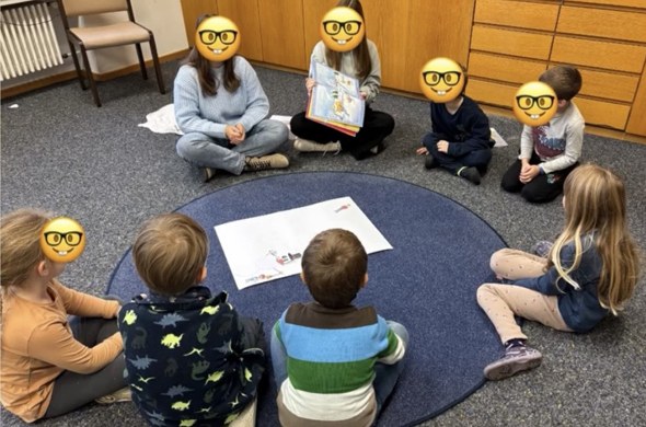 Schulkinder sitzen am Boden im Kreis und lauschen